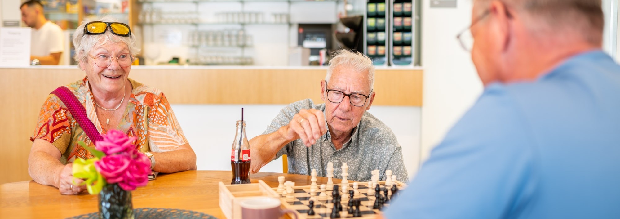 Twee mannen zijn aan het schaken en een vrouw kijkt toe.