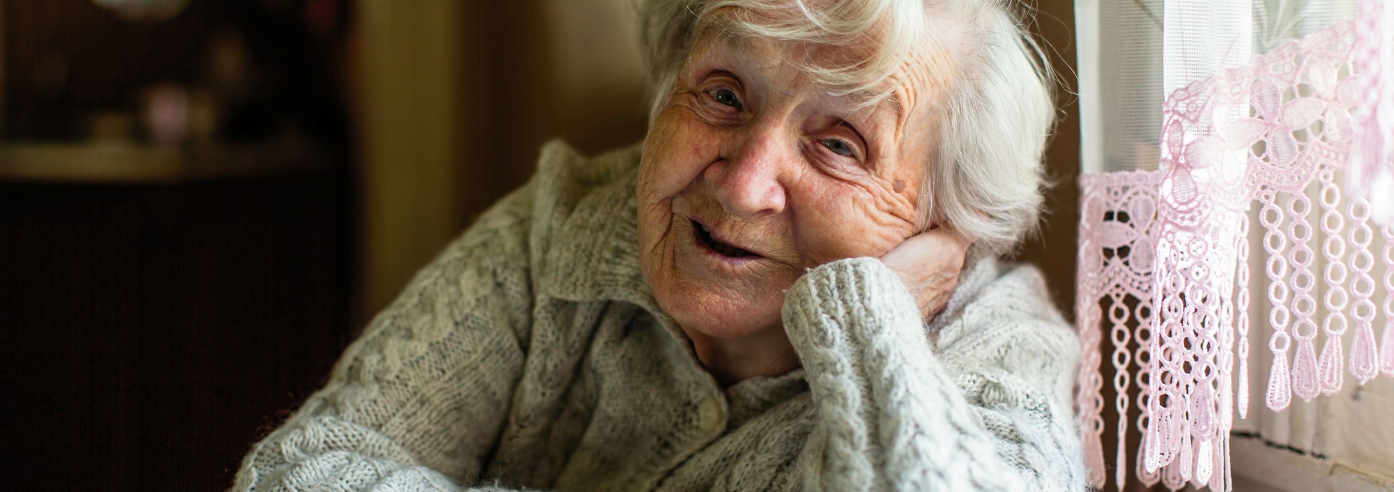Vrouw met wit haar houdt hand onder hoofd en lacht.