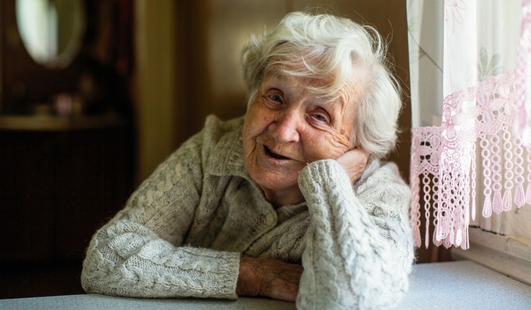 Vrouw met wit haar houdt hand onder hoofd en lacht.