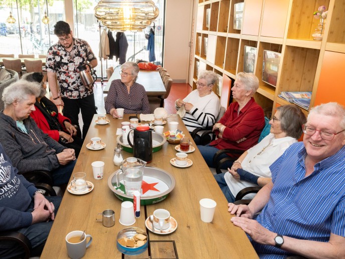 Groep oudere mensen zit aan tafel en drinkt.