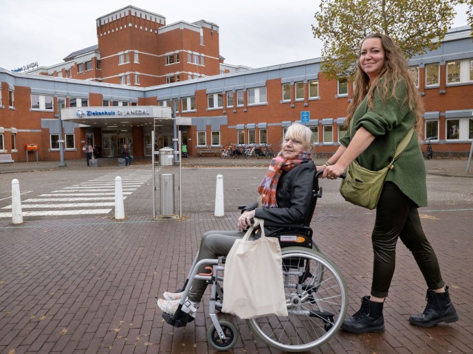 Vrouw duwt andere vrouw in rolstoel naar het ziekenhuis