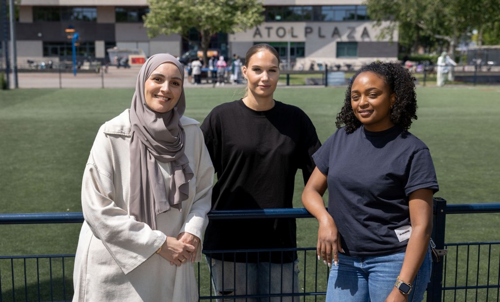 Drie vrouwen staan voor een hek.