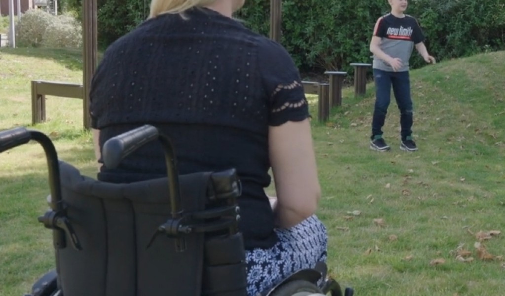 Vrouw in rolstoel is in speeltuin met kind.