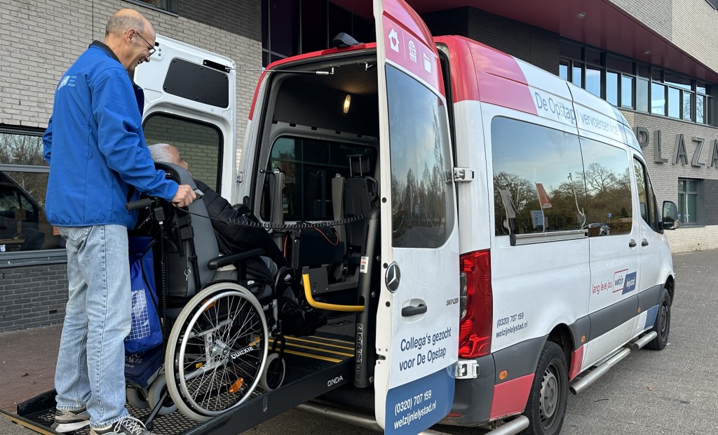 Chauffeur van De Opstap helpt mevrouw in rolstoel in de bus.