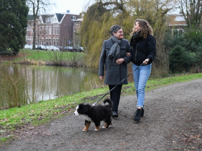 Een meisje haakt haar arm door die van een oudere vrouw en laat samen met haar de hond uit,
