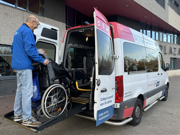 Chauffeur van de Opstap helpt een mevrouw in de rolstoel de bus in.