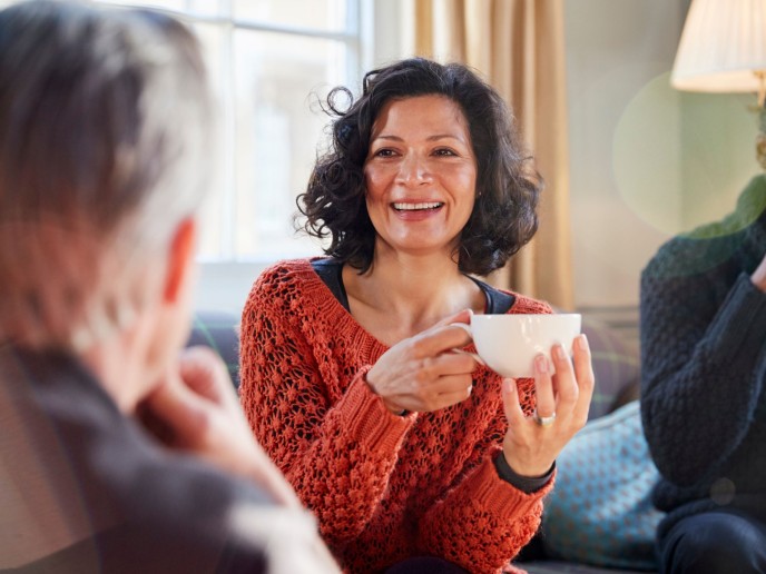 Vrouw houdt kopje koffie vast en lacht naar een ander.