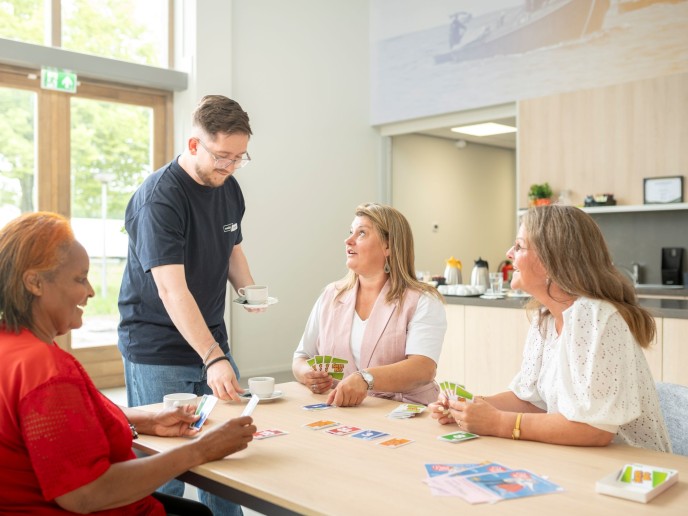 Drie vrouwen zittem aan tafel en man schenkt koffie in.
