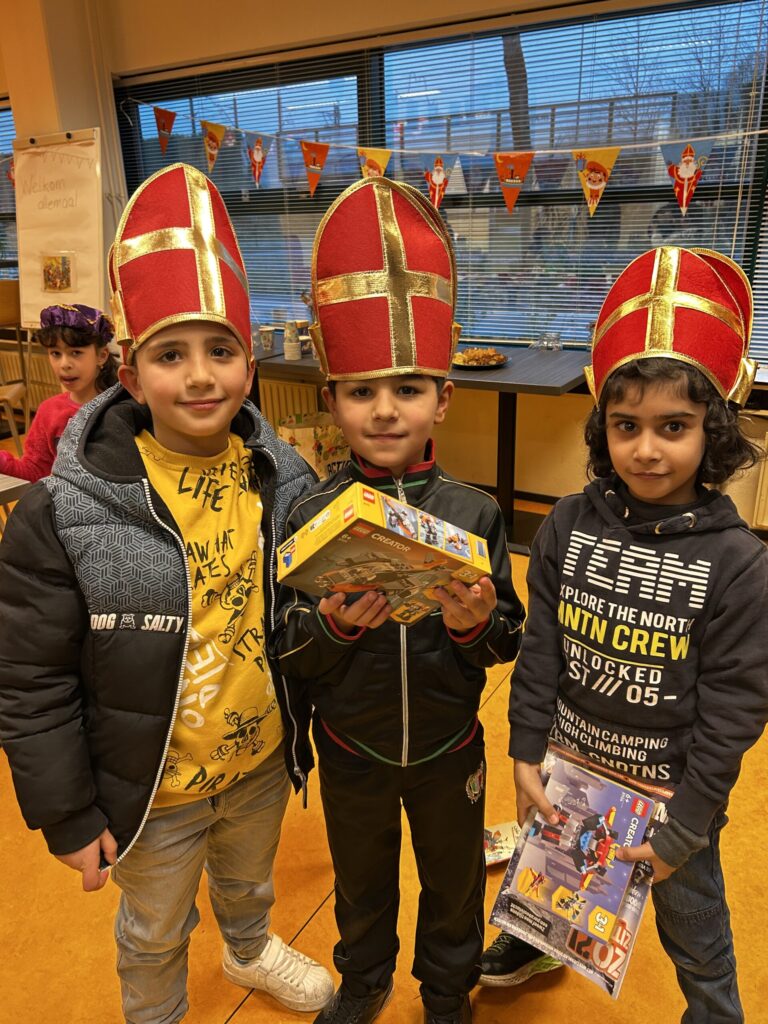 Drie jonge kinderen met een mijter van Sinterklaas op. Ze hebben een cadeautje vast.